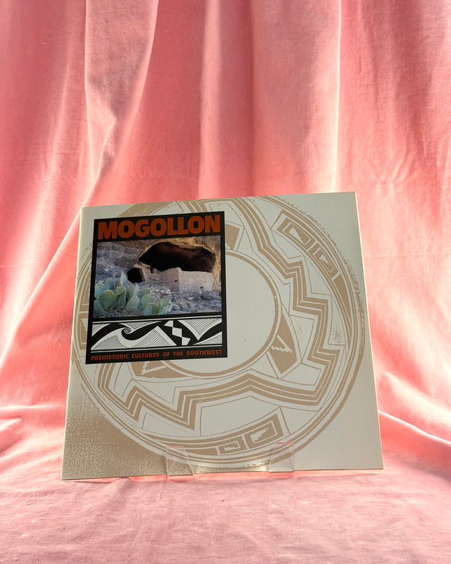 Book or notebook with a cover featuring the word 'Mogollon' and a circular design on a pink fabric background