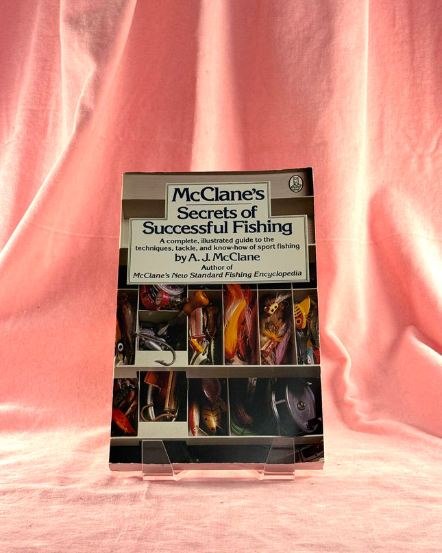 Book titled 'McClane's Secrets of Successful Fishing' on a pink fabric background
