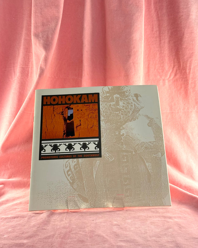 Book or album cover with 'HOHOKAM' text and illustrations on a pink fabric background