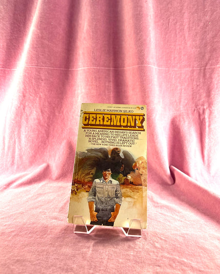 Book cover of 'Ceremony' by Leslie Marmon Silko on a pink fabric background