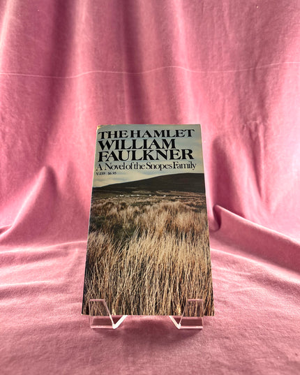 Book titled 'The Hamlet' by William Faulkner on a pink fabric background