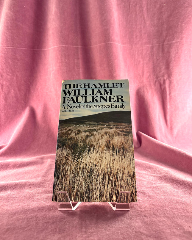 Book titled 'The Hamlet' by William Faulkner on a pink fabric background