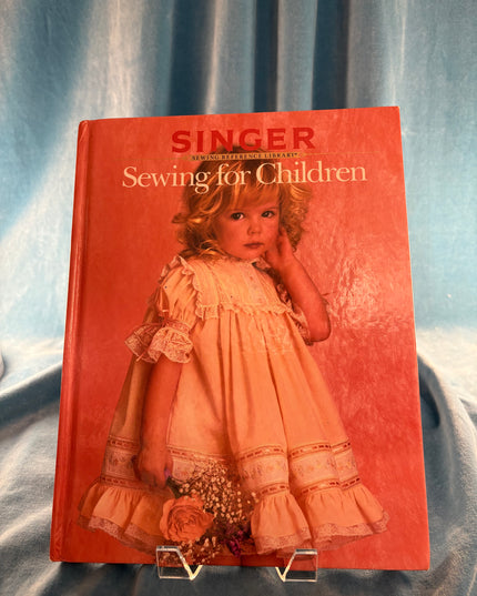 Book titled 'Sewing for Children' by Singer with a doll on the cover, placed on a textured surface.