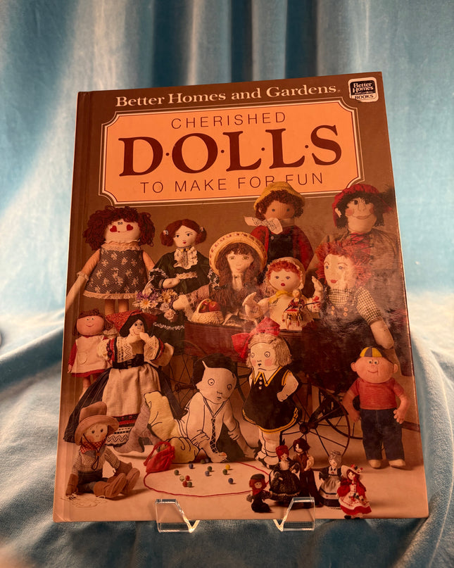 Book cover of 'Cherished Dolls' with illustrations of dolls on a blue fabric background