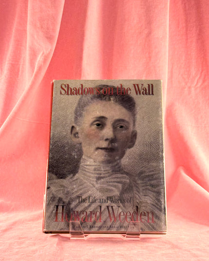 Book titled 'Shadow on the Wall: The Life and Works of Howard Weeden' on a pink fabric background