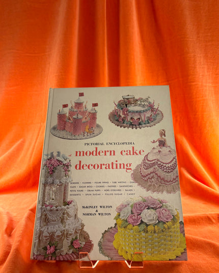 Book titled 'Pictorial Encyclopedia of Modern Cake Decorating' on an orange background