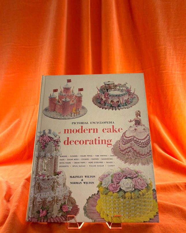 Book titled 'Pictorial Encyclopedia of Modern Cake Decorating' on an orange background