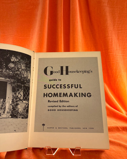 Open book titled 'Good Housekeeping's Guide to Successful Homemaking' on an orange fabric background