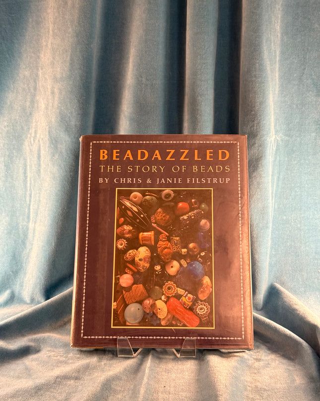 Book titled 'Beadazzled: The Story of Beads' by Chris & Janie Filstrup on a textured fabric background