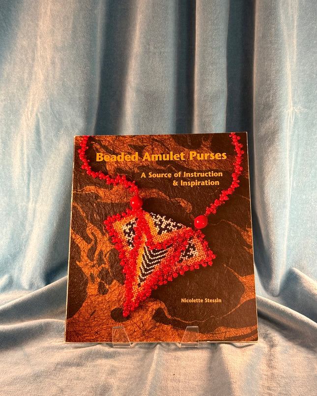 Book titled 'Beaded Amulet Purses' on a textured fabric background