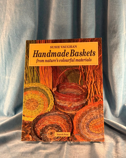 Book titled 'Handmade Baskets from nature's colourful materials' by Susie Vaughan on a textured fabric background