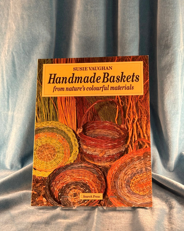 Book titled 'Handmade Baskets from nature's colourful materials' by Susie Vaughan on a textured fabric background