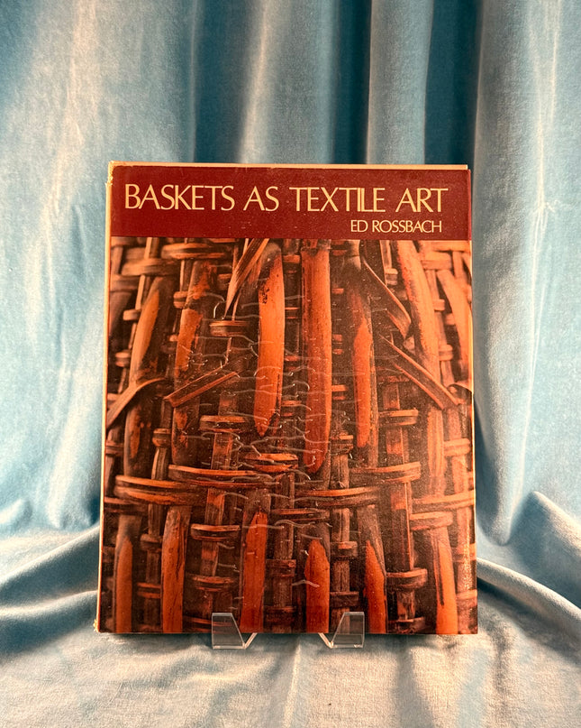 Book titled 'Baskets as Textile Art' by Ed Rossbach on a textured fabric background