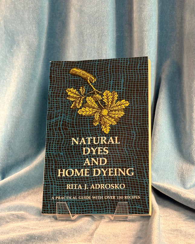 Book titled 'Natural Dyes and Home Dyeing' by Rita J. Adrosko on a textured fabric background