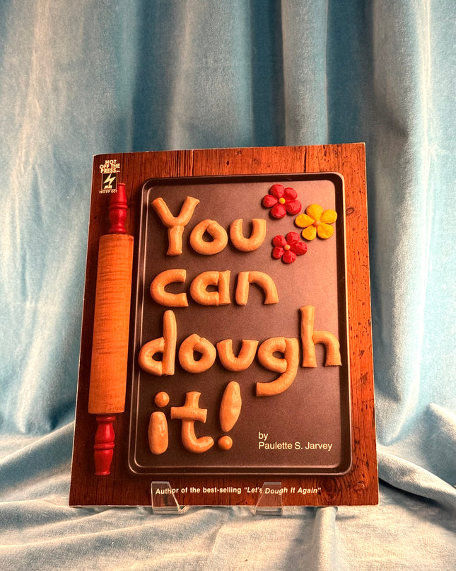 Wooden book-shaped mold with 'You can dough it!' text and rolling pin on a blue fabric background