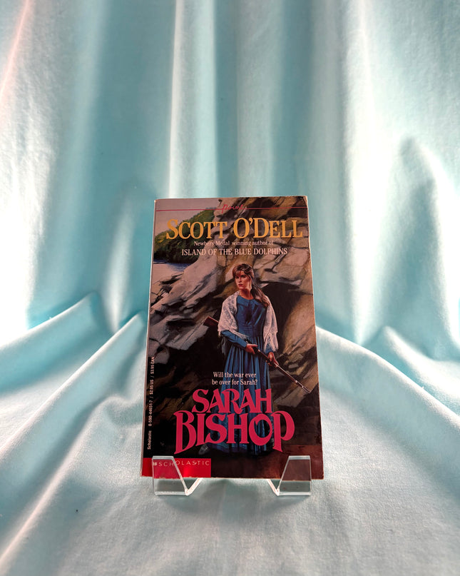 Book titled 'Sarah Bishop' by Scott O'Dell on a stand against a light blue curtain background.