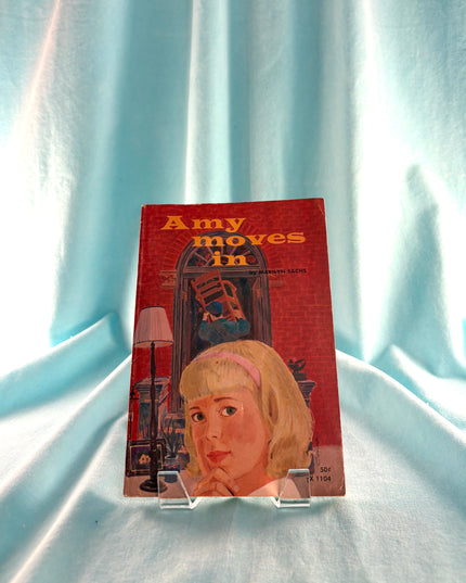 Vintage book titled 'Amy Moves In' on a light blue fabric background