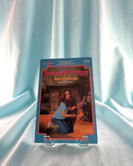 Book titled 'Nobody's Orphan' by Anne Lindbergh on a clear stand against a light blue curtain background