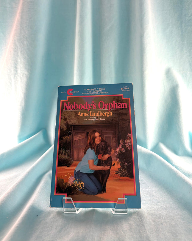 Book titled 'Nobody's Orphan' by Anne Lindbergh on a clear stand against a light blue curtain background