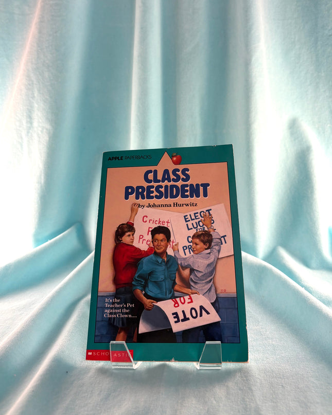 Book titled 'Class President' on a stand against a light blue curtain background