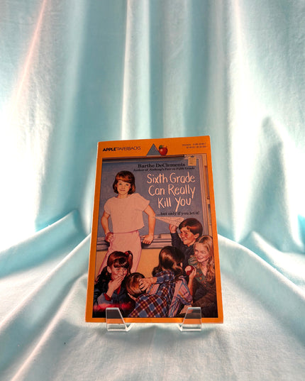 Book cover of 'Sixth Grade Can Really Kill You' on a stand against a light curtain background