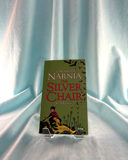 Book titled 'The Silver Chair' from 'The Chronicles of Narnia' series on a stand against a light curtain background.