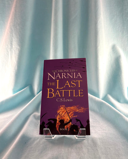 Book titled 'The Last Battle' from 'The Chronicles of Narnia' series on a stand against a light curtain background
