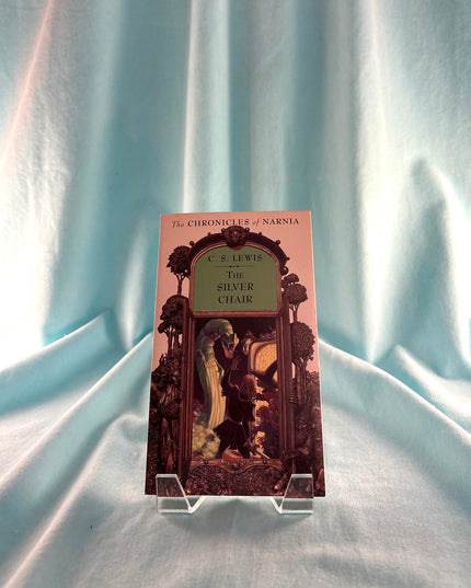 Book titled 'The Silver Chair' from 'The Chronicles of Narnia' series on a stand against a light blue curtain background.