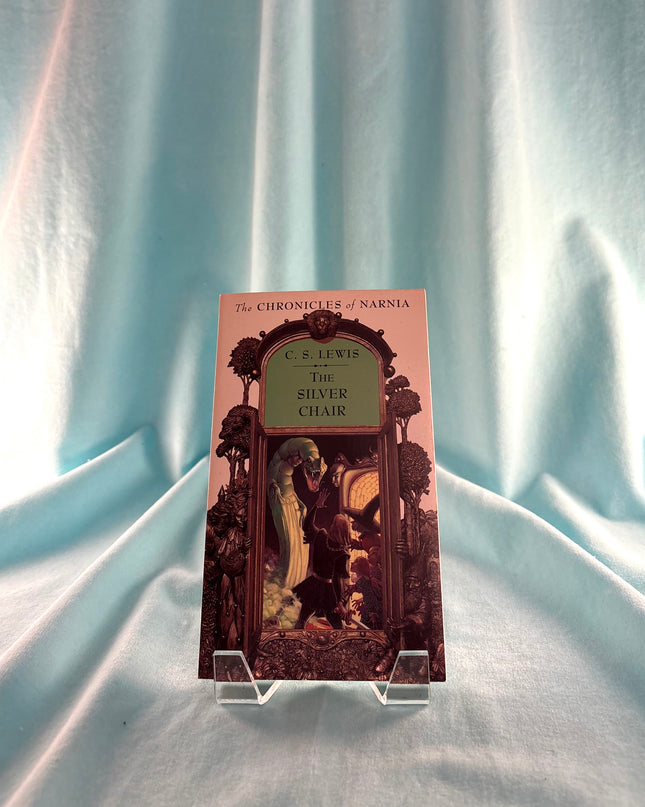 Book titled 'The Silver Chair' from 'The Chronicles of Narnia' series on a stand against a light blue curtain background.