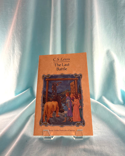 Book titled 'The Last Battle' by C.S. Lewis on a stand with a light blue curtain background