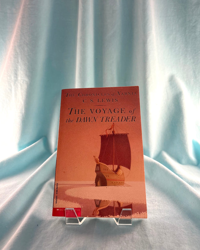 Book titled 'The Voyage of the Dawn Treader' by C.S. Lewis on a stand against a light blue fabric background fuzzy