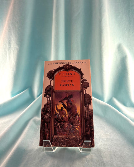 Book titled 'Prince Caspian' by C.S. Lewis on a stand against a light blue curtain background