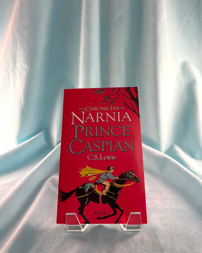Book titled 'Prince Caspian' by C.S. Lewis on a clear stand against a light curtain background