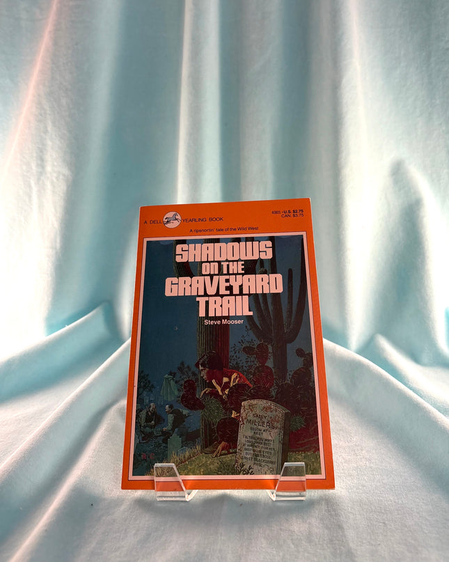 Book titled 'Shadows on the Graveyard Trail' on a light blue fabric background