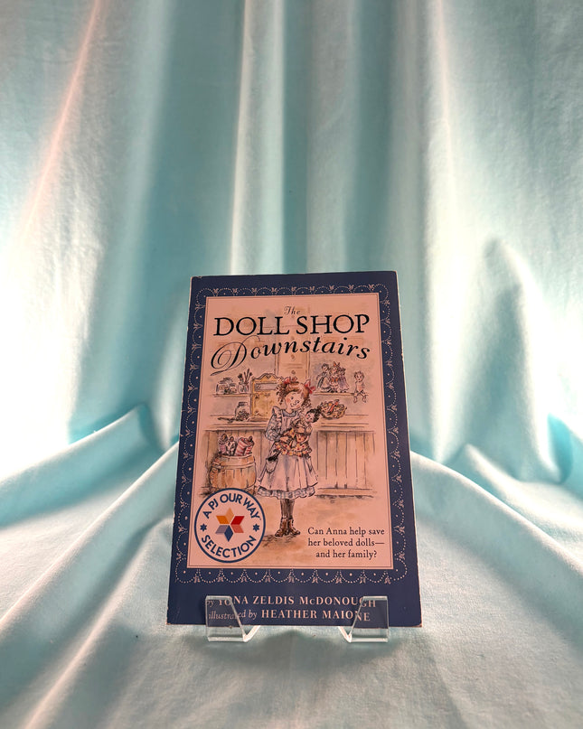 Book titled 'Doll Shop Downstairs' on a light blue fabric background
