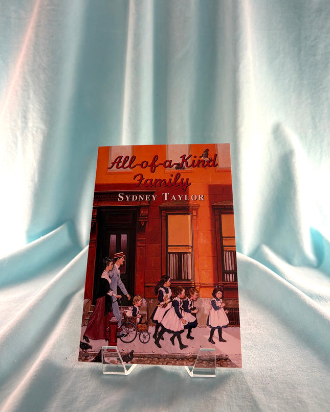 Book titled 'All of a Kind Family' by Sydney Taylor on a light blue fabric background