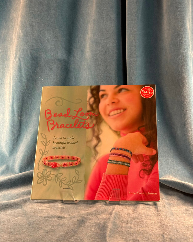Book titled 'Bead Loom Bracelets' with a girl on the cover against a gray curtain background