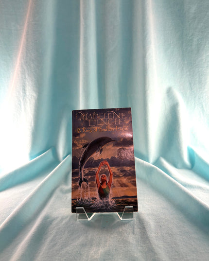 Book titled 'A Ring of Endless Light' on a stand against a light blue curtain background