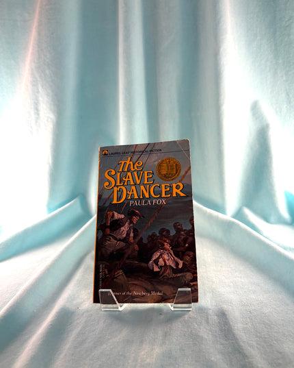 Book titled 'The Slave Dancer' by Paula Fox on a light blue fabric background