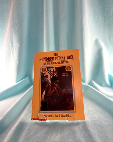 Book titled 'The Hundred Penny Box' by Sharon Bell Mathis on a light blue fabric background