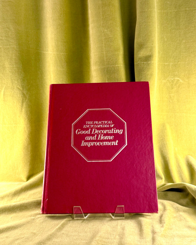 Red book titled 'The Practical Encyclopedia of Good Decorating and Home Improvement' on a yellow fabric background