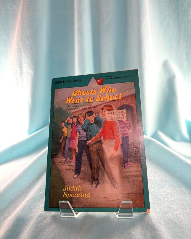 Book titled 'Ghosts Who Went to School' by Judith Spearing on a stand against a light curtain background