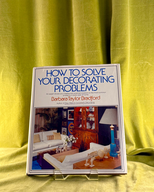 Book titled 'How to Solve Your Decorating Problems' by Barbara Taylor Bradford on a green fabric background