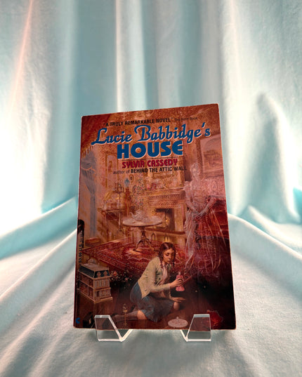 Book titled 'Lucie Babbidge's House' on a clear stand against a white curtain background