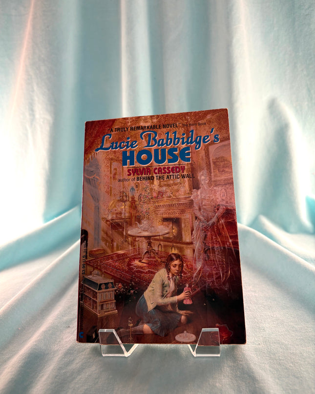 Book titled 'Lucie Babbidge's House' on a clear stand against a white curtain background