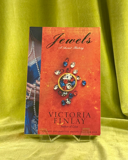 Book cover of 'Jewels' by Victoria Finlay on a green fabric background