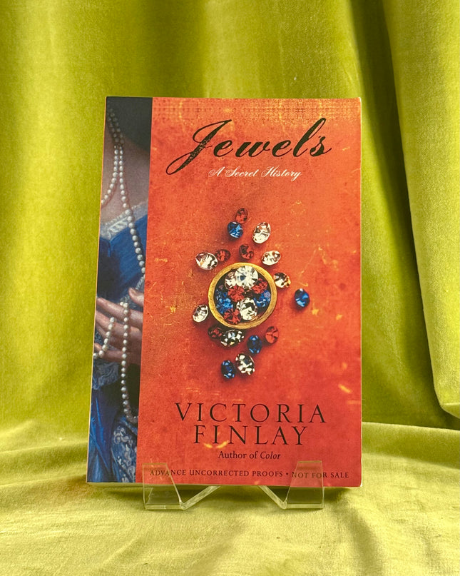 Book cover of 'Jewels' by Victoria Finlay on a green fabric background
