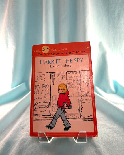 Book cover of 'Harriet the Spy' by Louise Fitzhugh on a stand against a light curtain background