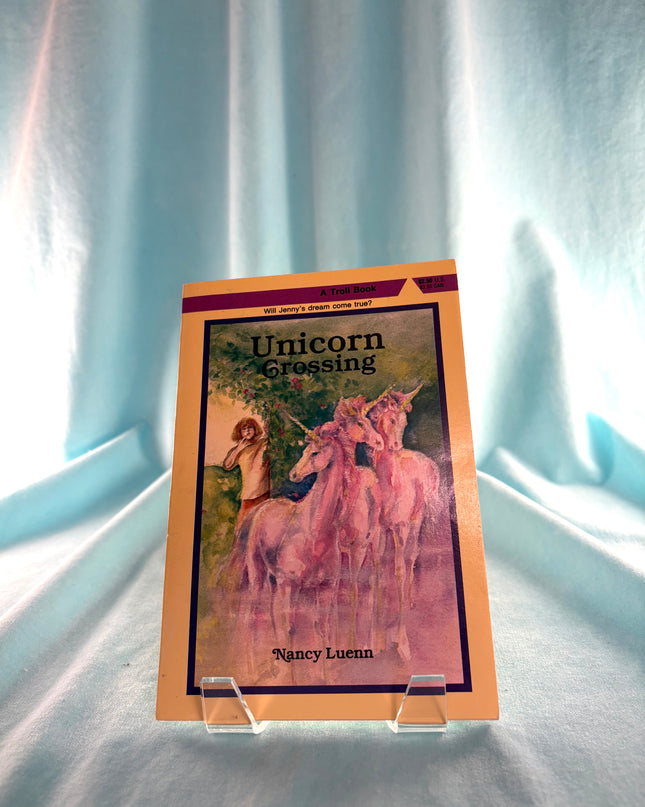 Book titled 'Unicorn Crossing' by Nancy Luenn on a clear stand against a light curtain background