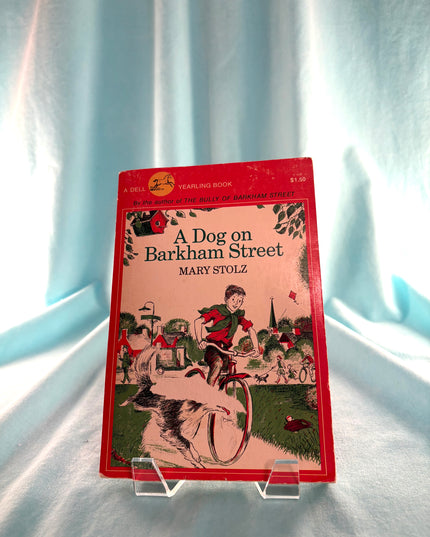 Book titled 'A Dog on Barkham Street' by Mary Stolz on a clear stand against a light blue curtain background.